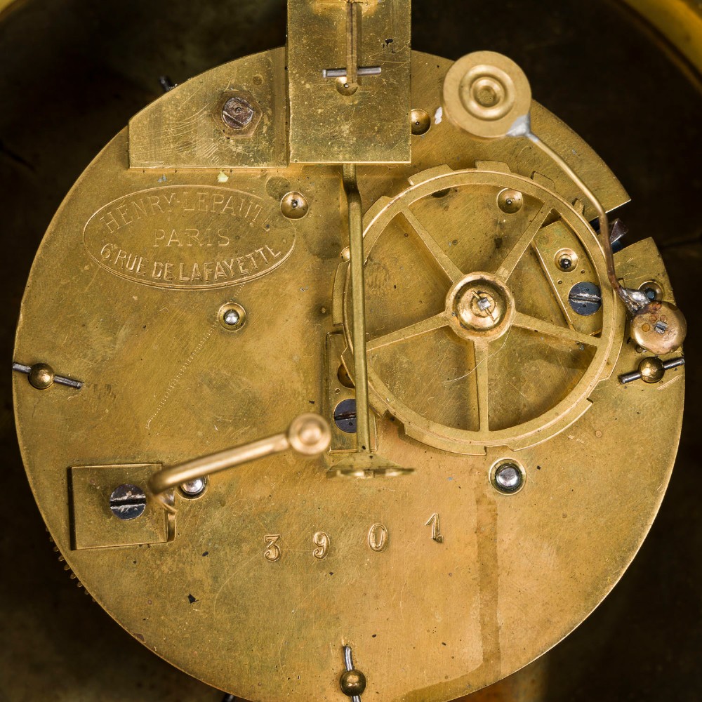 A circular dark bronze French wall clock designed in the shape of a pocket watch with a white enamel dial and Roman numerals. View IX