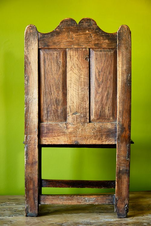 A late 17th-century dark oak armchair featuring a panelled backrest, shaped crest rail, curved armrests, rectangular wooden seat, and square legs with low stretchers. View V