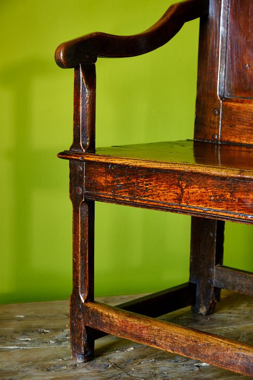 A late 17th-century dark oak armchair featuring a panelled backrest, shaped crest rail, curved armrests, rectangular wooden seat, and square legs with low stretchers. View VI