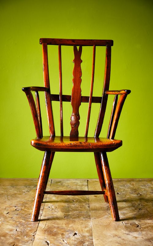 A primitive wooden Windsor armchair crafted from varied native hardwoods featuring a solid carved seat, shaped central back splat, tapered spindles, and splayed legs. View II