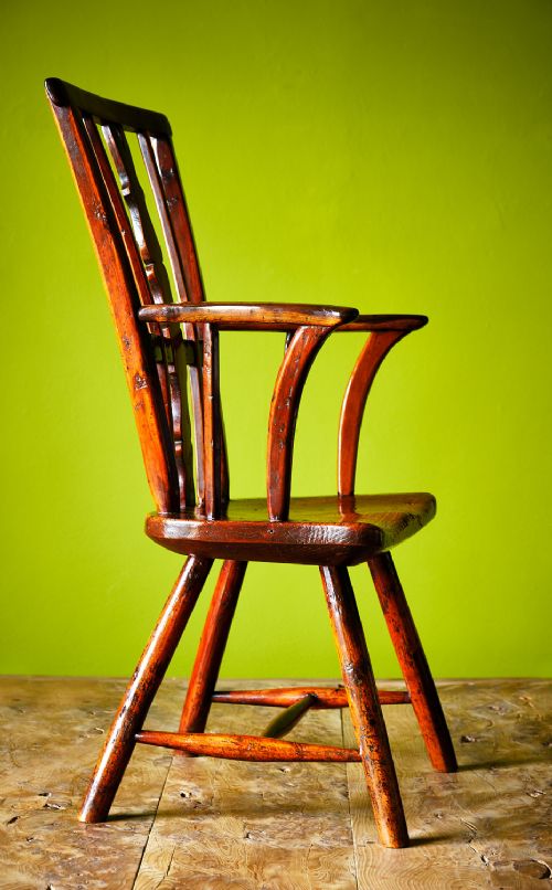 A primitive wooden Windsor armchair crafted from varied native hardwoods featuring a solid carved seat, shaped central back splat, tapered spindles, and splayed legs. View III