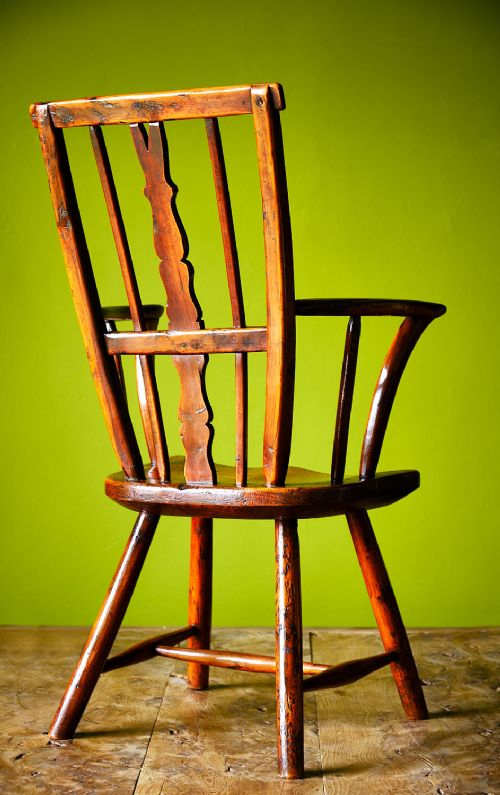 A primitive wooden Windsor armchair crafted from varied native hardwoods featuring a solid carved seat, shaped central back splat, tapered spindles, and splayed legs. View IV