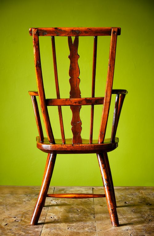 A primitive wooden Windsor armchair crafted from varied native hardwoods featuring a solid carved seat, shaped central back splat, tapered spindles, and splayed legs. View V