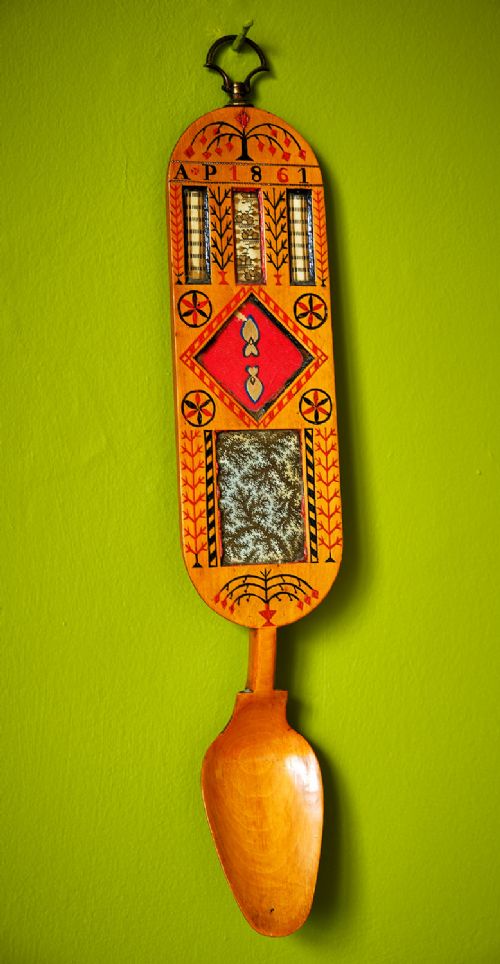 A carved wooden Welsh love spoon featuring polychrome wax inlay, glazed inset panels, incised initials AP, the date 1861, and a brass suspension loop at the top. View II