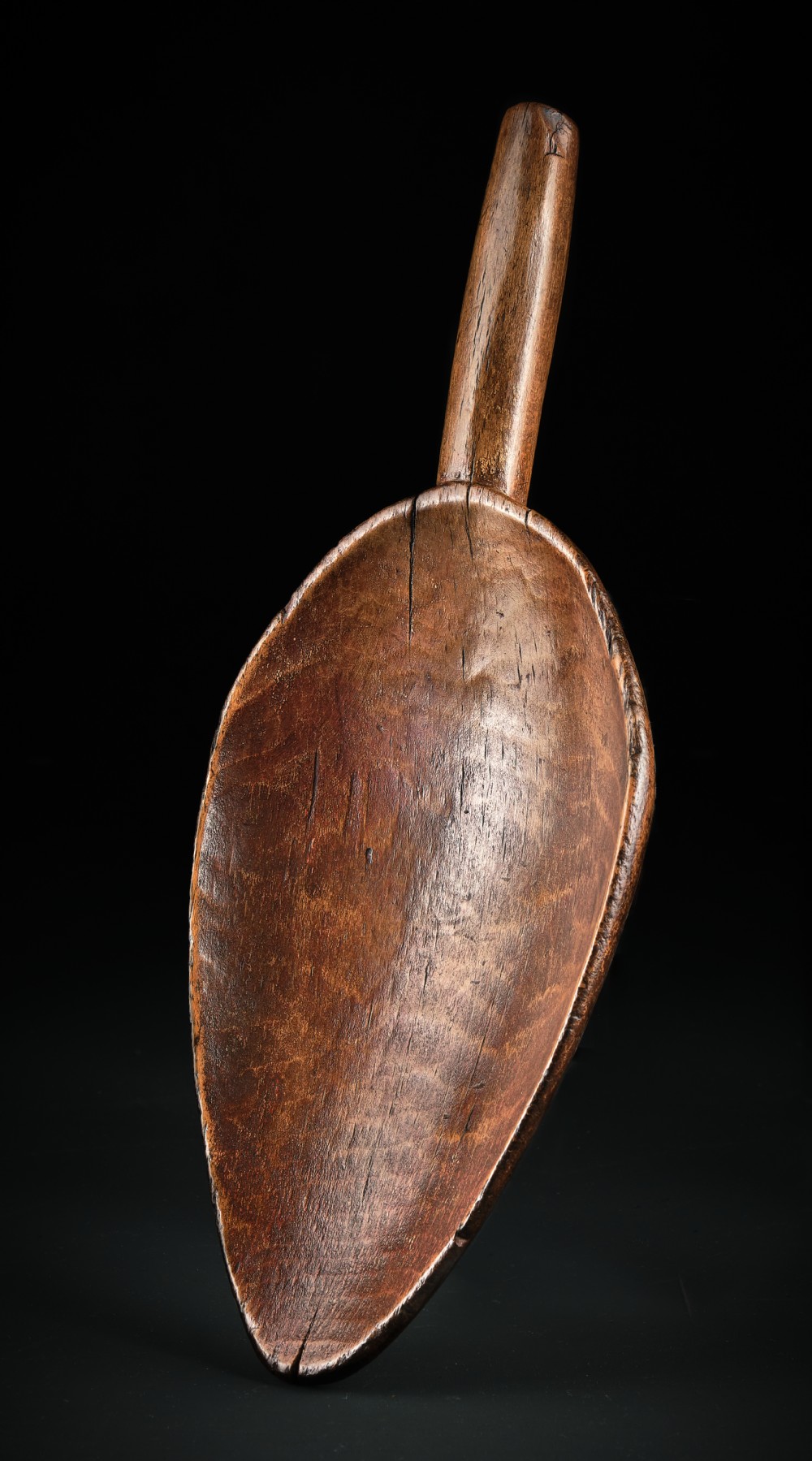 A hand-carved dark beechwood flour and grain scoop with a tapered cylindrical handle and rich patinated surface.