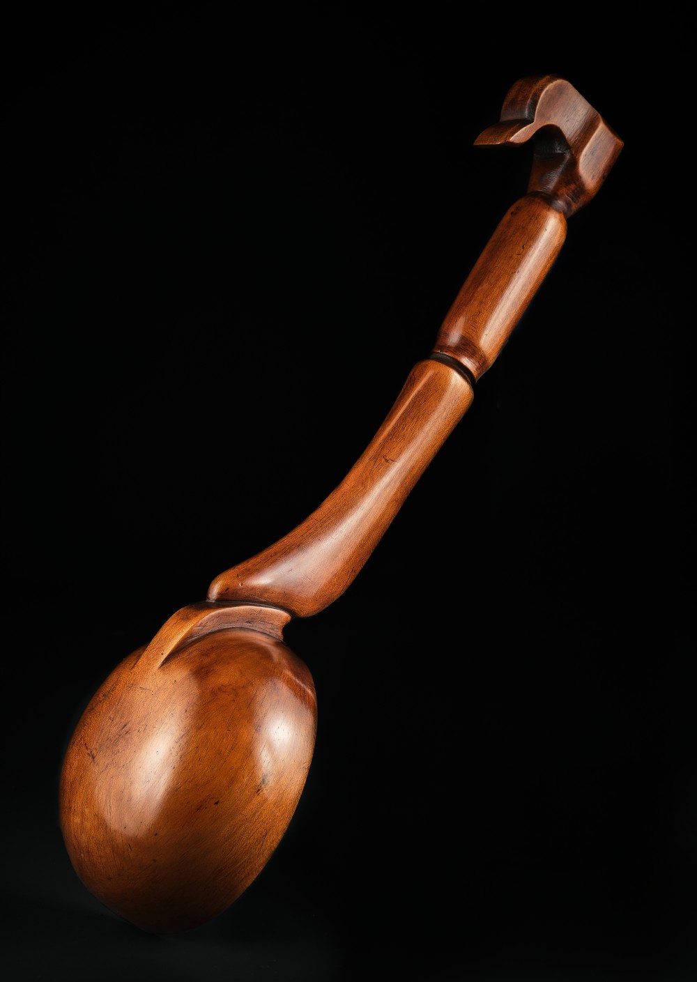 A hand-carved antique Welsh cherrywood ladle featuring a deep oval bowl, curved handle, and hooked terminal.