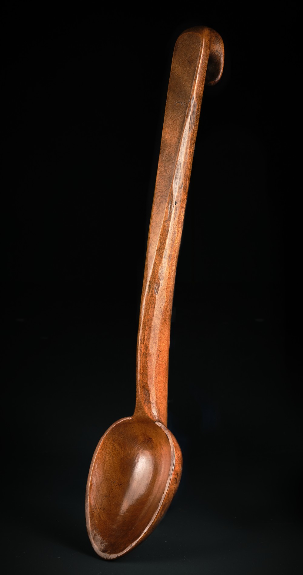 A hand-carved antique Welsh sycamore wooden ladle featuring an oval bowl and a long handle terminating in a hook.