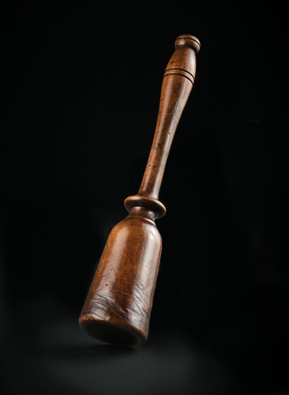 A turned dark brown sycamore wood potato masher featuring a contoured handle and bulbous head with visible age patina.
