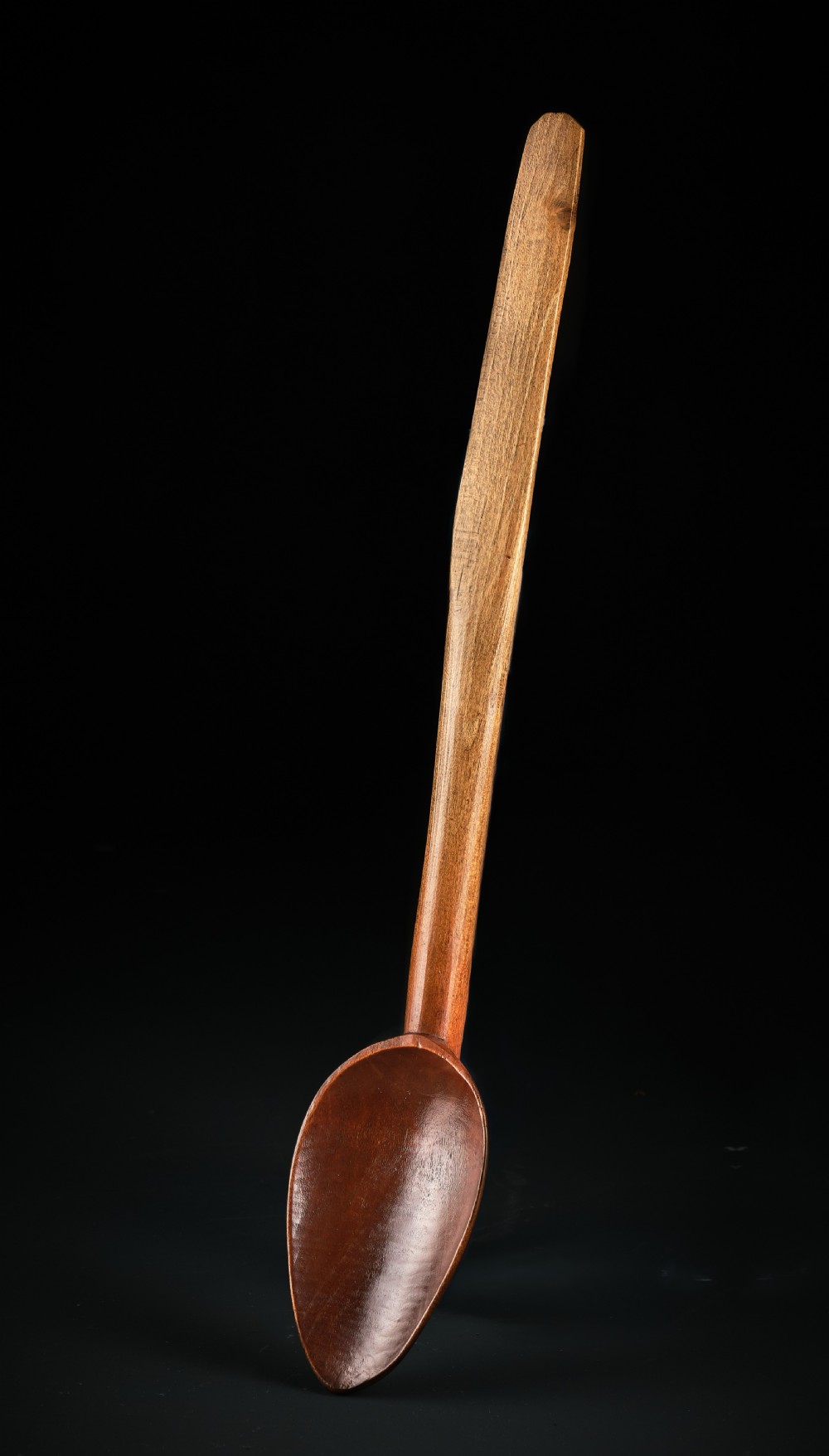 A long-handled Georgian beechwood basting spoon with a carved oval bowl against a black background.