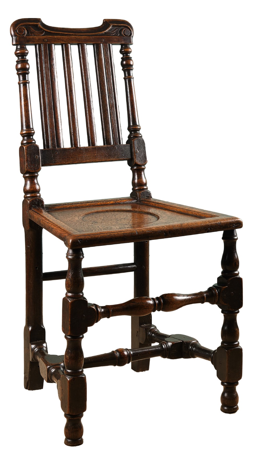 A late 17th-century dark oak side chair featuring turned legs, vertical back slats, and a carved crest rail.