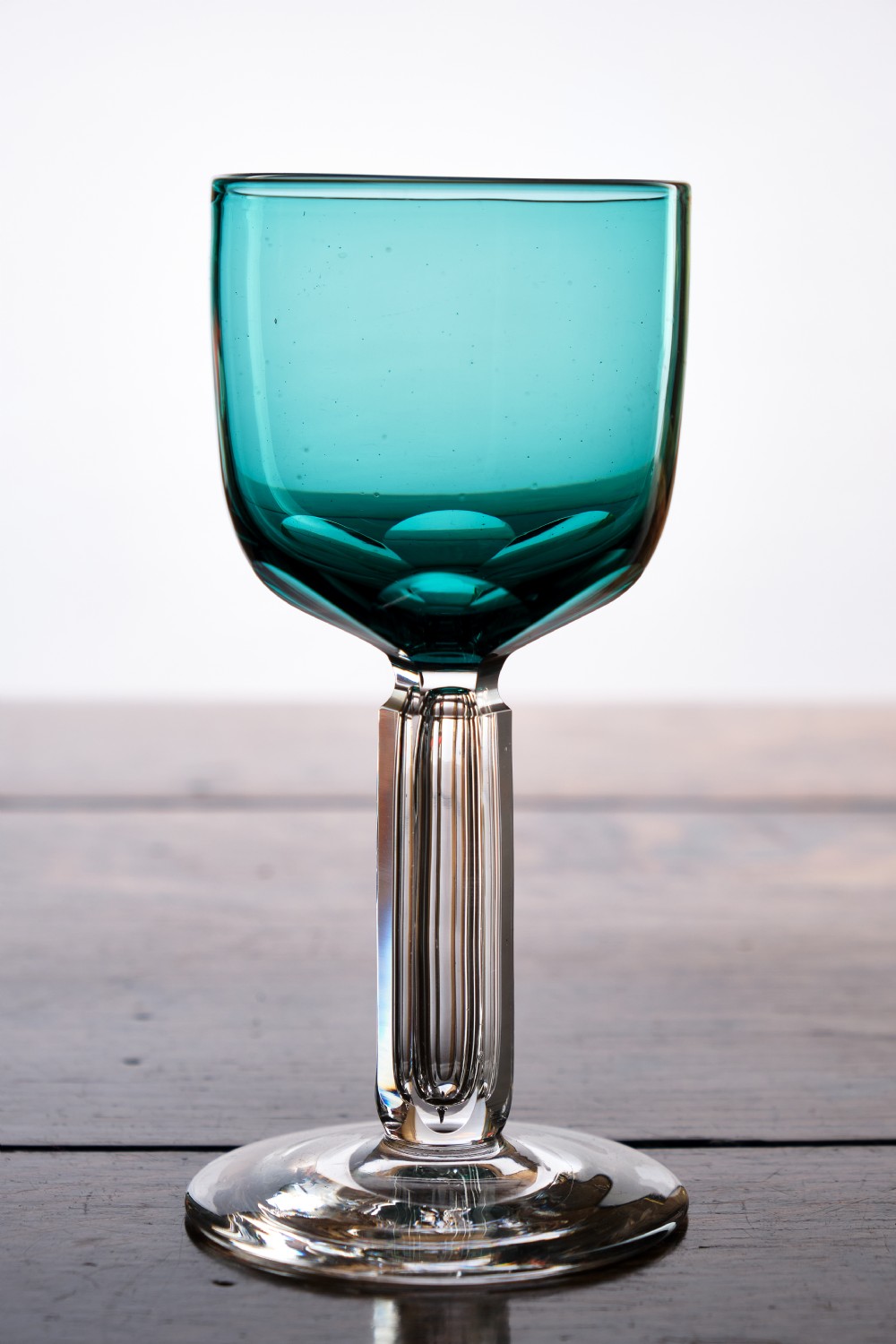 A Victorian teal glass stemware piece featuring a round coloured bowl and a clear faceted cut stem on a circular base.