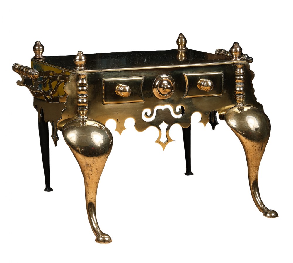 A polished brass Welsh footman hearth trivet with cabriole front legs, turned finials, carrying handles, and a pierced apron. View II