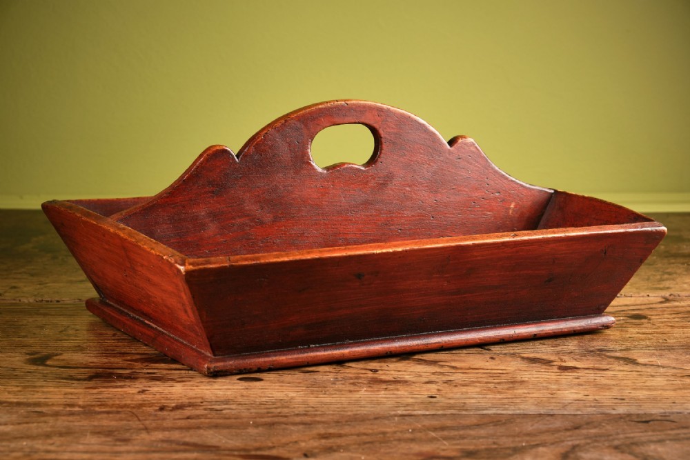 A red-painted wooden knife tray featuring a central divider with an integrated oval handle cut-out and shaped cresting.