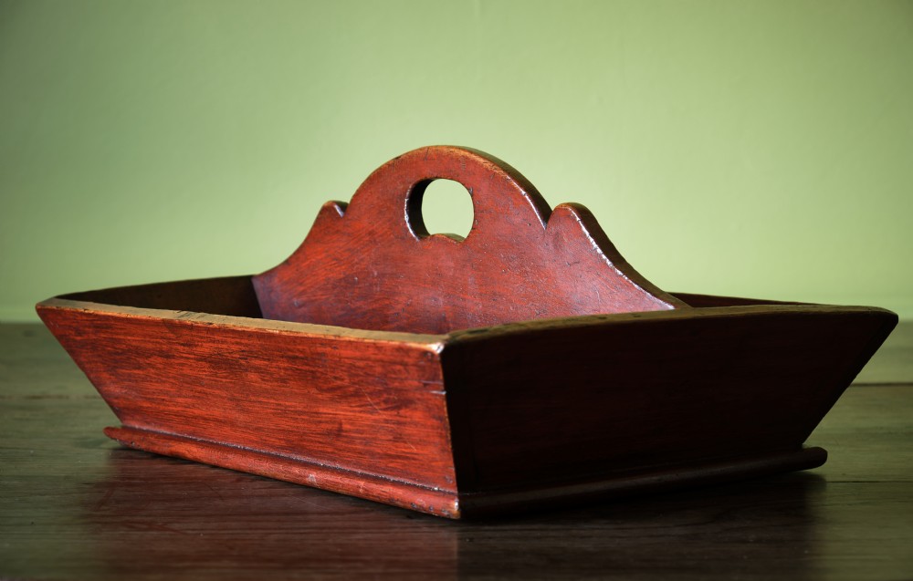 A red-painted wooden knife tray featuring a central divider with an integrated oval handle cut-out and shaped cresting. View V