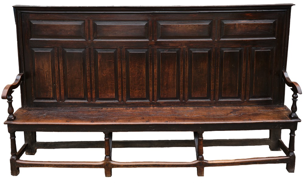A high-backed dark oak settle with fielded panelling across the backrest, turned front legs, and a long wooden seat. View II