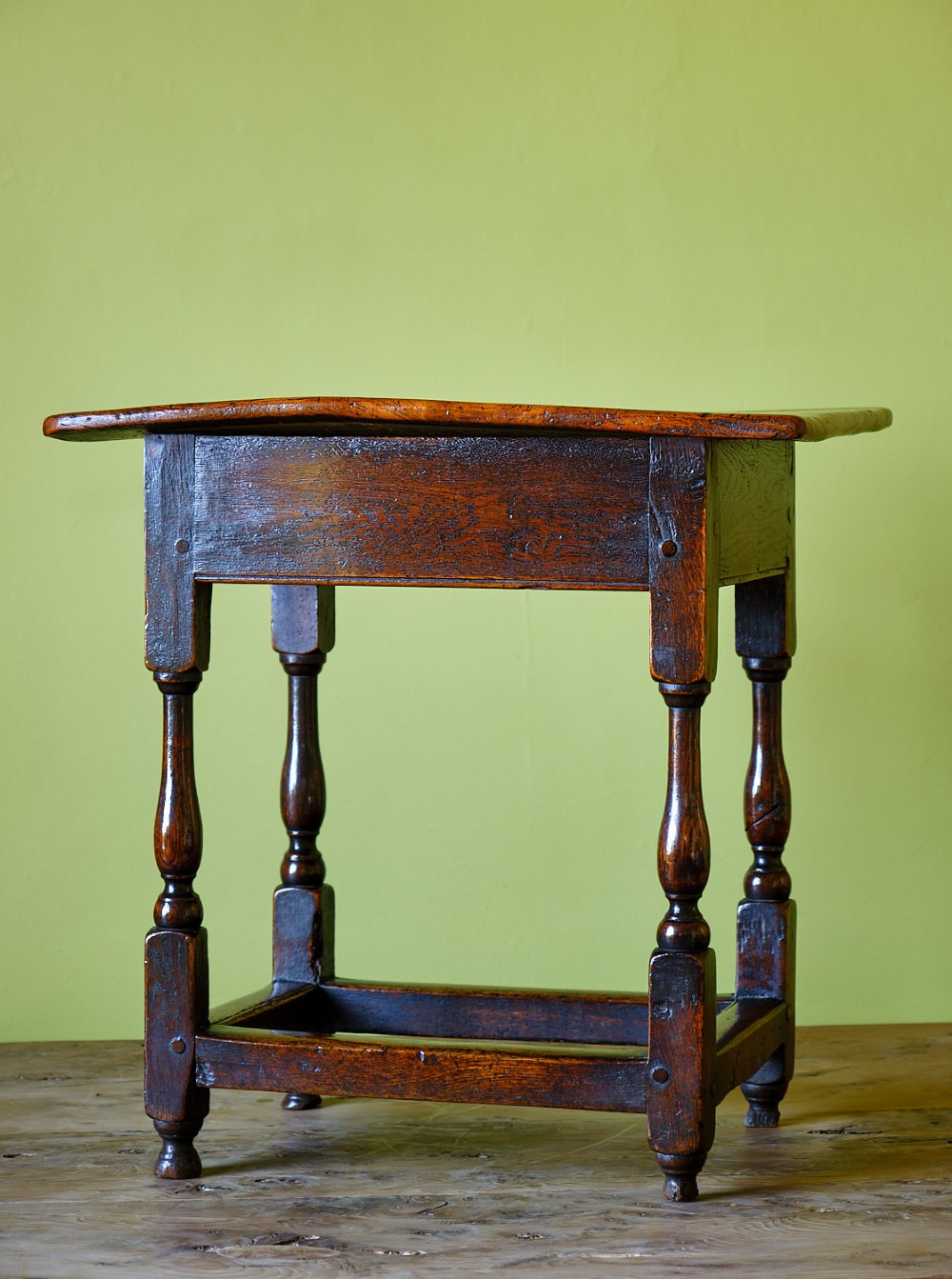 A small early 18th-century dark oak and elm occasional table featuring turned legs, a plank top, and lower stretchers.