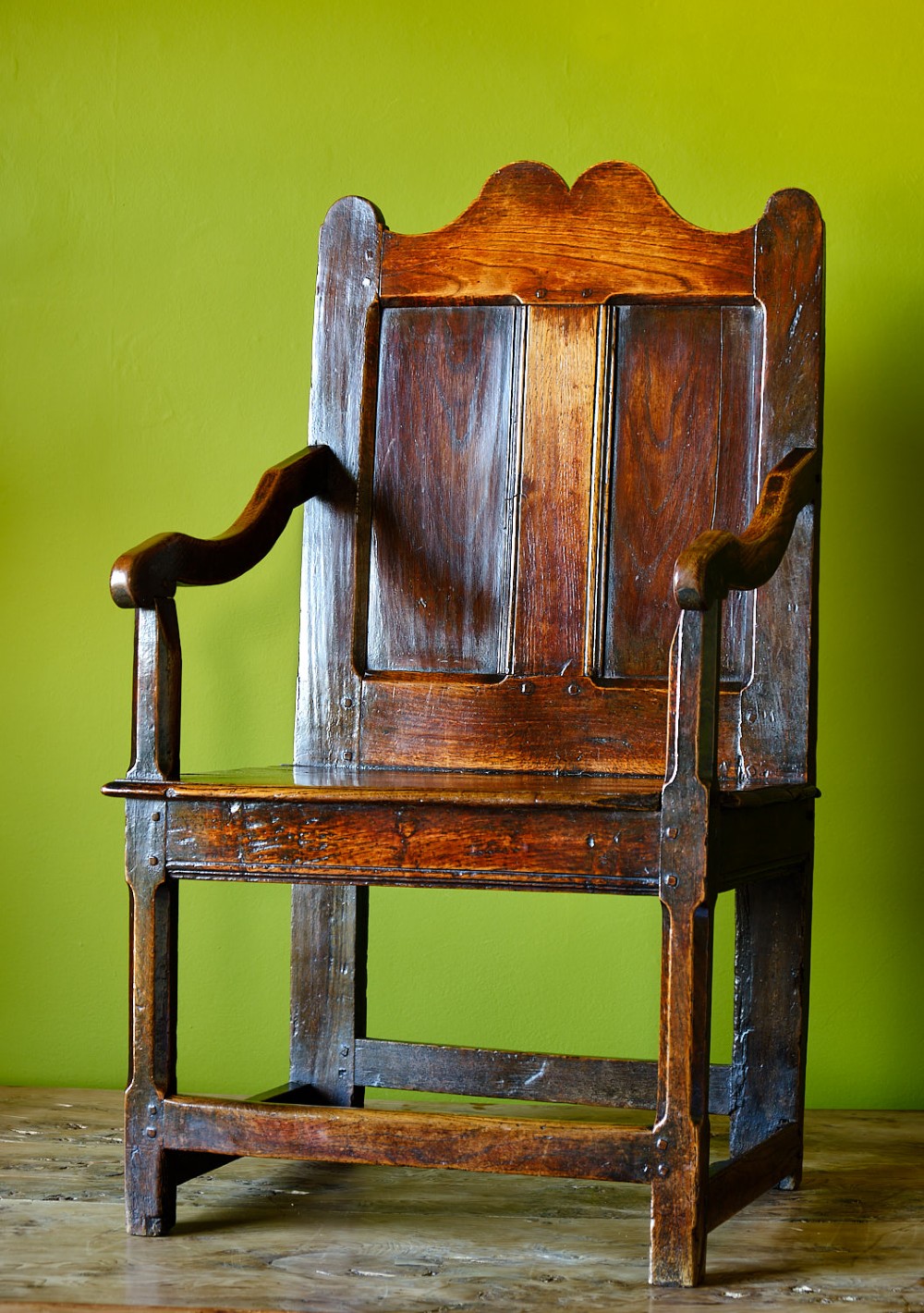 A late 17th-century dark oak armchair featuring a panelled backrest, shaped crest rail, curved armrests, rectangular wooden seat, and square legs with low stretchers.