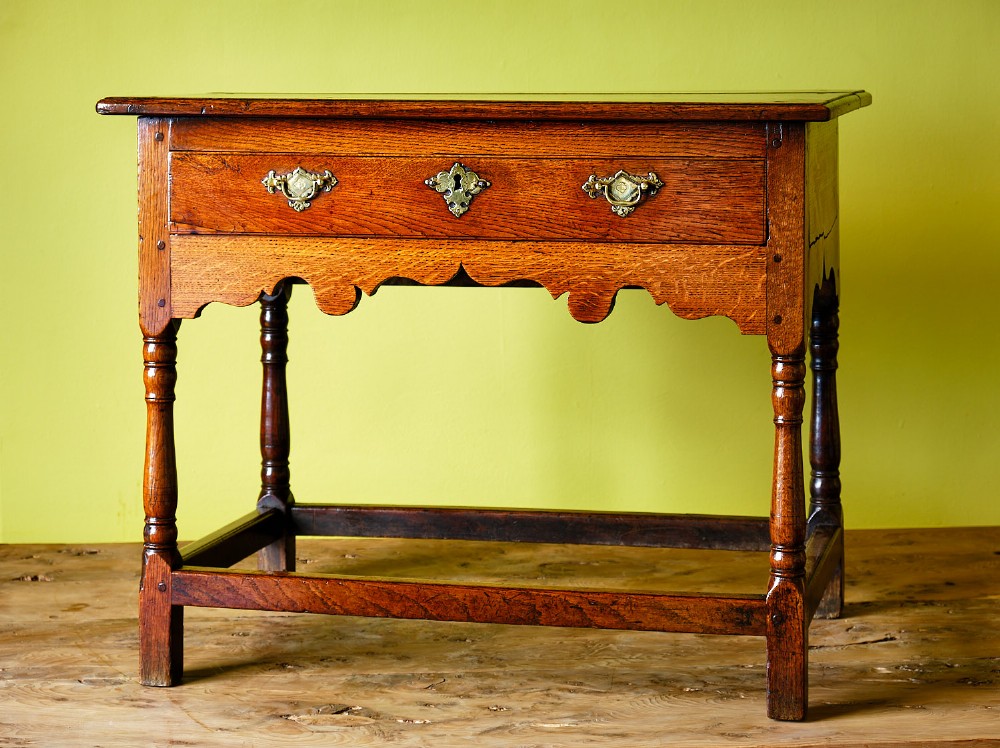A Georgian oak side table featuring a single drawer with brass handles, a scalloped apron below, turned legs, and a perimeter stretcher.