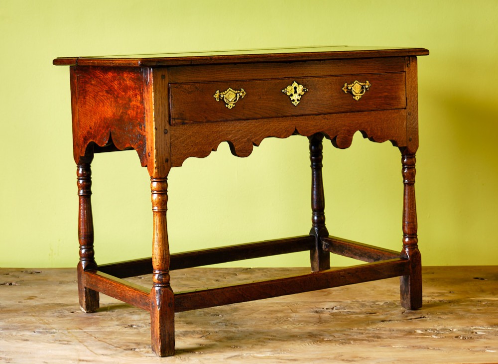 A Georgian oak side table featuring a single drawer with brass handles, a scalloped apron below, turned legs, and a perimeter stretcher. View II