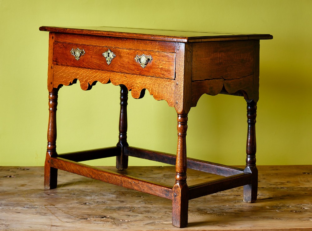 A Georgian oak side table featuring a single drawer with brass handles, a scalloped apron below, turned legs, and a perimeter stretcher. View III