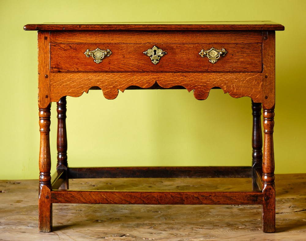 A Georgian oak side table featuring a single drawer with brass handles, a scalloped apron below, turned legs, and a perimeter stretcher. View VII