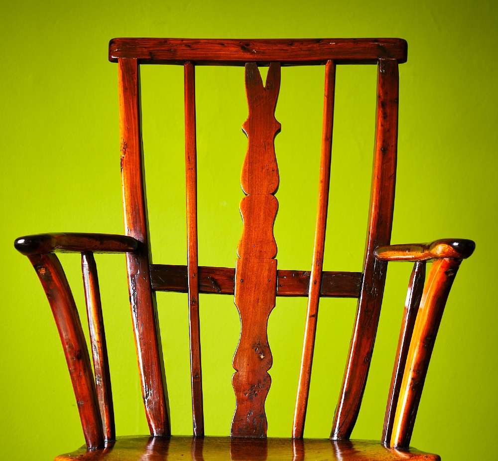 A primitive wooden Windsor armchair crafted from varied native hardwoods featuring a solid carved seat, shaped central back splat, tapered spindles, and splayed legs. View VI