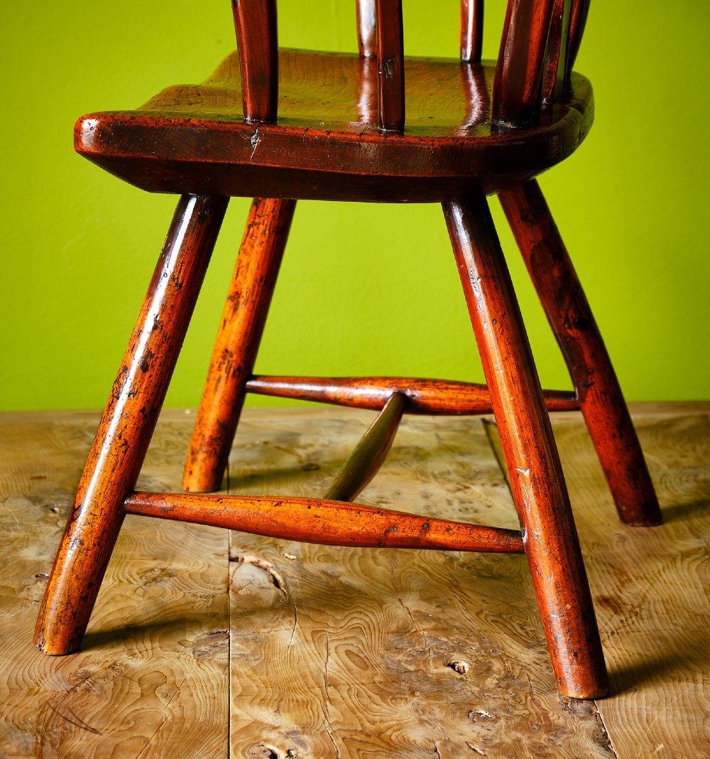 A primitive wooden Windsor armchair crafted from varied native hardwoods featuring a solid carved seat, shaped central back splat, tapered spindles, and splayed legs. View X