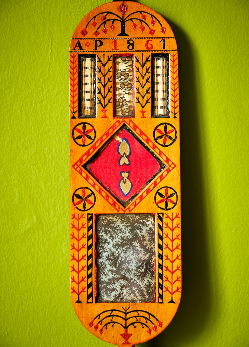 A carved wooden Welsh love spoon featuring polychrome wax inlay, glazed inset panels, incised initials AP, the date 1861, and a brass suspension loop at the top. View III