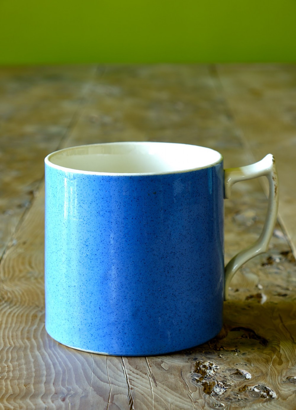 A large cylindrical ceramic mug featuring a speckled blue glazed exterior and a light cream interior with a matching handle.