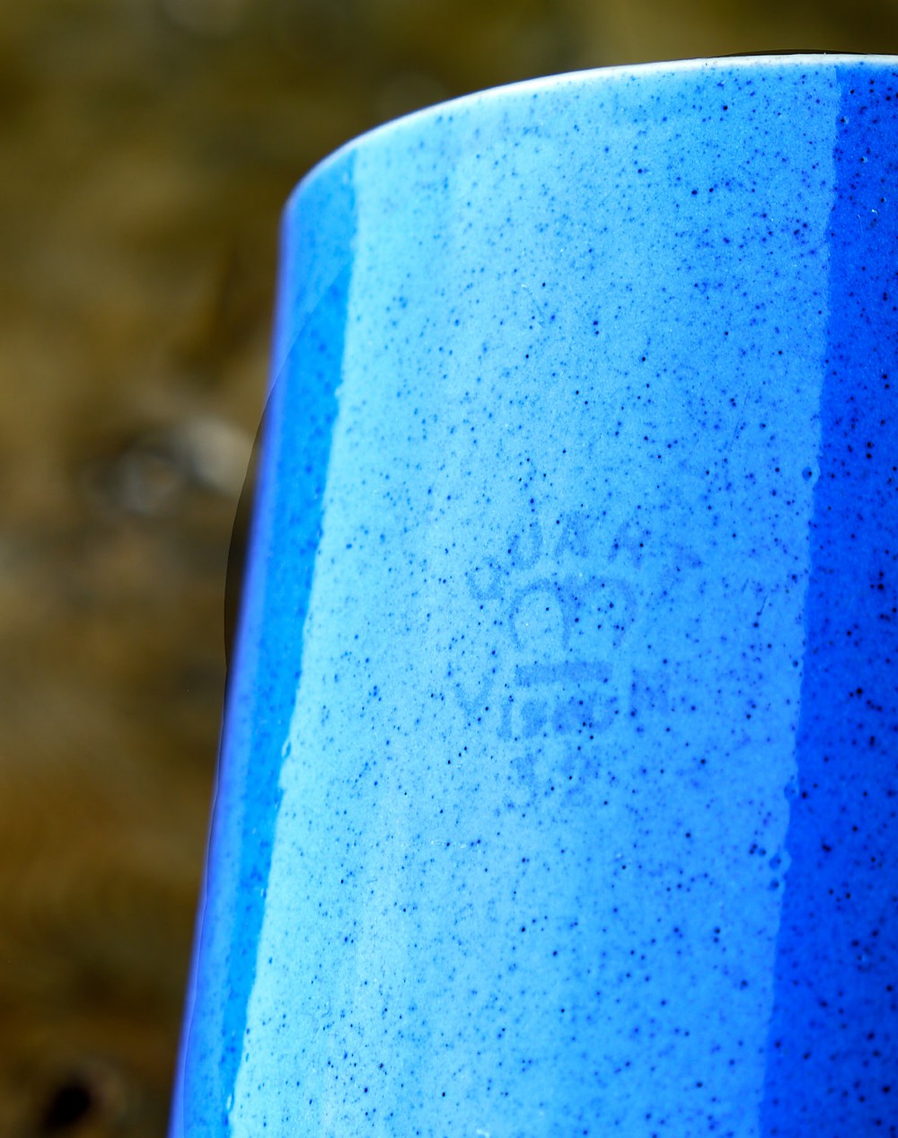 A large cylindrical ceramic mug featuring a speckled blue glazed exterior and a light cream interior with a matching handle. View V