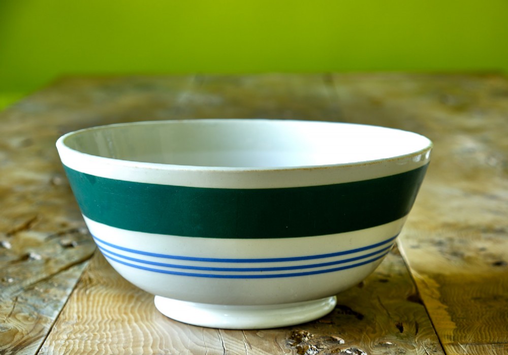 A white ceramic mixing bowl featuring a wide horizontal green band near the rim and three thin blue stripes around the lower body.