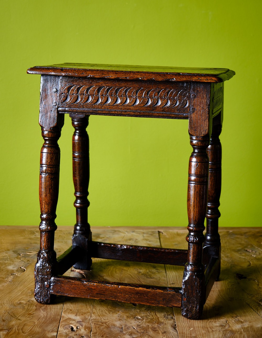 A dark oak seventeenth-century joined stool with a rectangular top, carved apron frieze, turned legs, and low box stretchers.