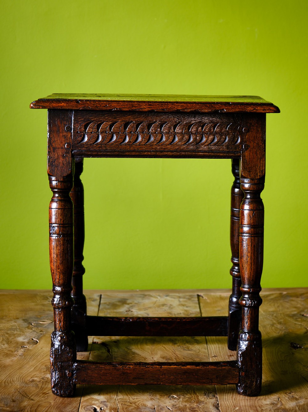 A dark oak seventeenth-century joined stool with a rectangular top, carved apron frieze, turned legs, and low box stretchers. View II