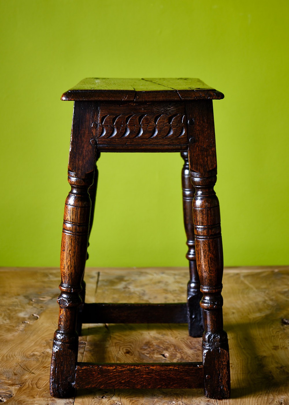 A dark oak seventeenth-century joined stool with a rectangular top, carved apron frieze, turned legs, and low box stretchers. View III