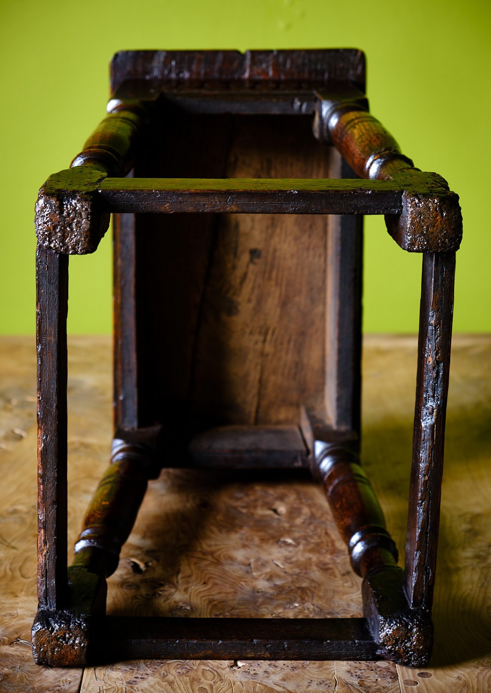 A dark oak seventeenth-century joined stool with a rectangular top, carved apron frieze, turned legs, and low box stretchers. View V
