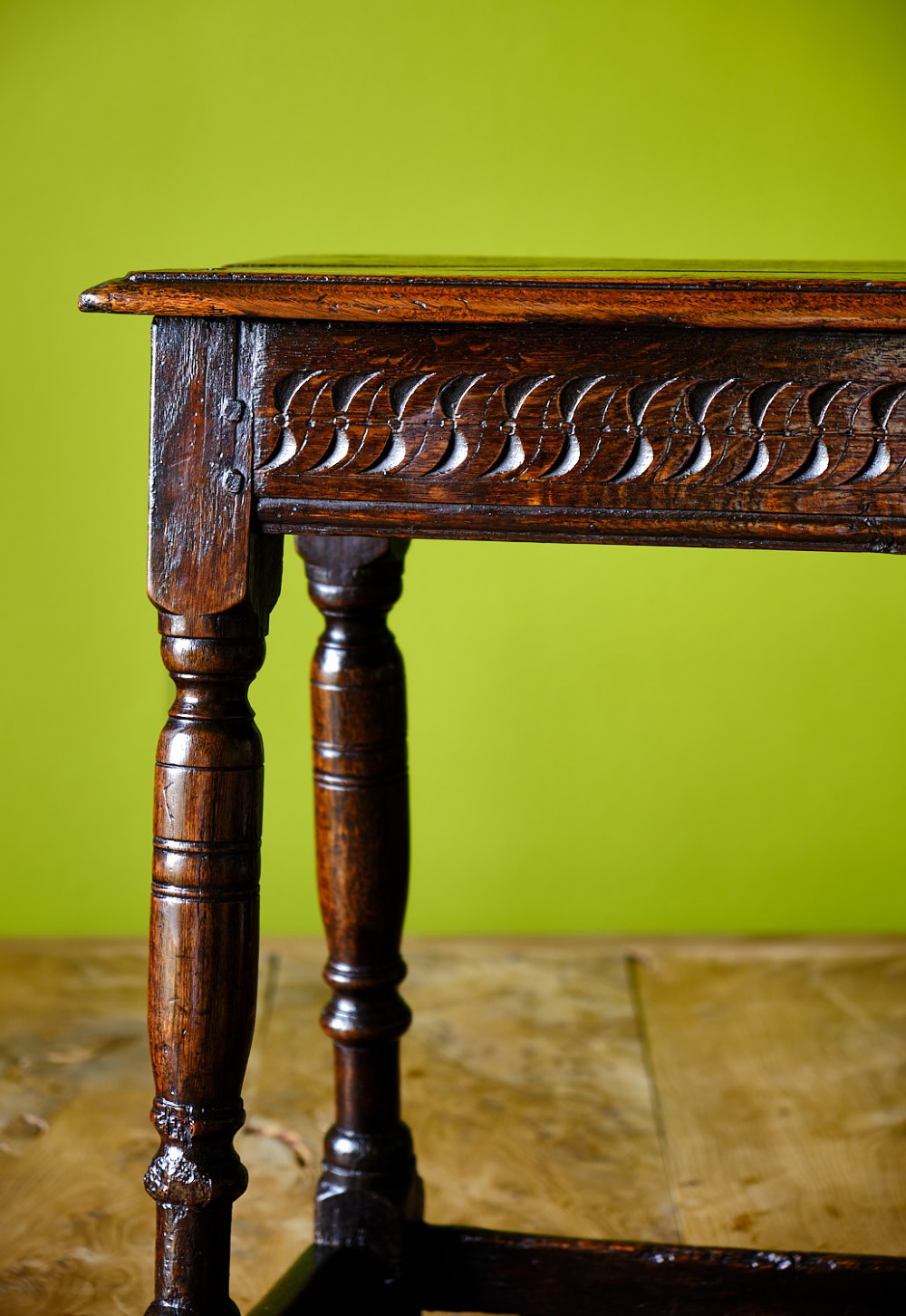 A dark oak seventeenth-century joined stool with a rectangular top, carved apron frieze, turned legs, and low box stretchers. View VI