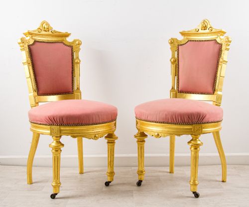 fig 1. A pair of antique French giltwood salon chairs featuring carved cresting, pink velvet upholstered seats and backs, and fluted front legs on castors.