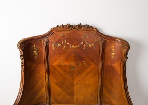 fig 1. An antique French wooden bed frame featuring a high curved headboard, wrapped footboard, parquetry veneer, and hand-painted floral swags.