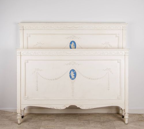 fig 1. An antique cream-painted French double bed frame featuring carved neoclassical swags, moulding, and central blue Jasperware-style oval plaques.