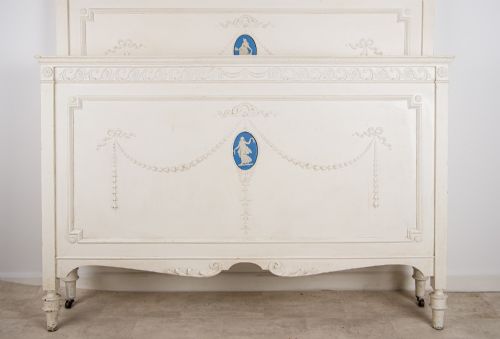 fig 2. An antique cream-painted French double bed frame featuring carved neoclassical swags, moulding, and central blue Jasperware-style oval plaques.