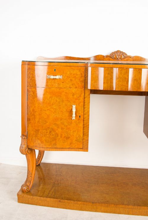 fig 2. An Art Deco burr walnut sideboard featuring two outer pedestal cupboards, carved cabriole legs, a glass top, and a lower plinth base.