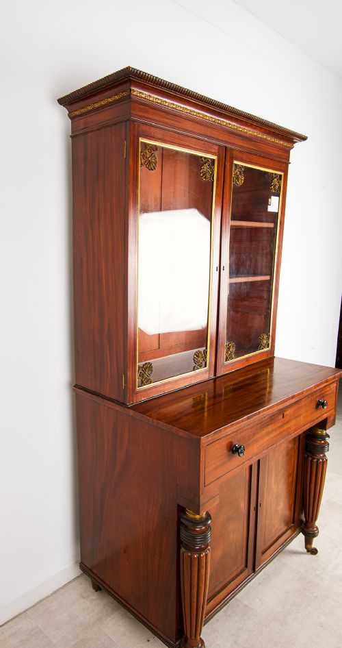 An antique Regency mahogany glazed bookcase cabinet with brass decorative mounts, fluted columns, and a lower two-door cupboard. View VII