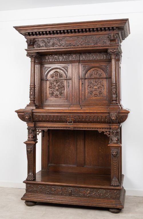 fig 1. A 19th-century carved oak buffet cupboard featuring intricate relief panels, architectural columns, an upper cabinet, and an open lower tier.