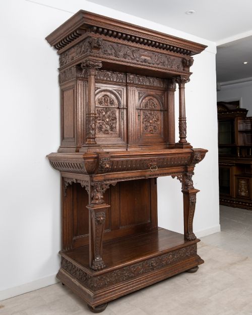 fig 2. A 19th-century carved oak buffet cupboard featuring intricate relief panels, architectural columns, an upper cabinet, and an open lower tier.