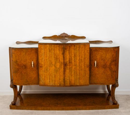 fig 1. An Art Deco burr walnut sideboard featuring a stepped top with a fluted central door, curved end cupboards, decorative handles, and carved legs resting on a continuous plinth.