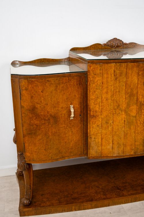 fig 2. An Art Deco burr walnut sideboard featuring a stepped top with a fluted central door, curved end cupboards, decorative handles, and carved legs resting on a continuous plinth.