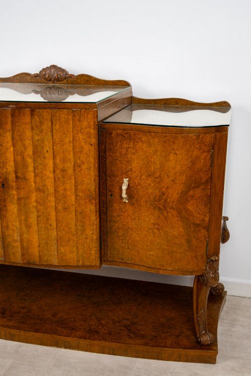 fig 3. An Art Deco burr walnut sideboard featuring a stepped top with a fluted central door, curved end cupboards, decorative handles, and carved legs resting on a continuous plinth.