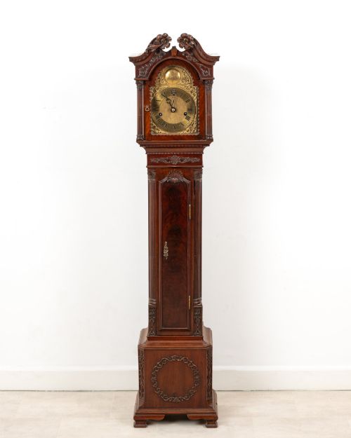 fig 1. An Edwardian mahogany grandmother clock with a carved swan neck pediment, a brass dial with Roman numerals, and a slim waist door.
