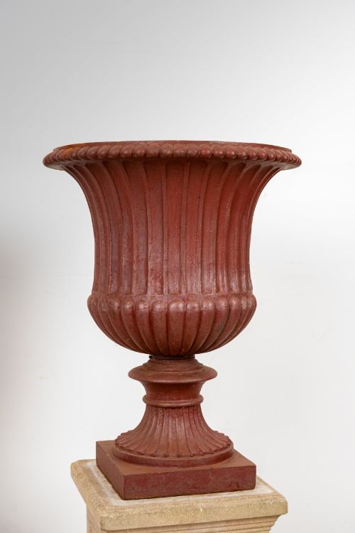 fig 2. A pair of 19th-century fluted cast iron Campana urns with rust-red finish, elevated on square carved beige stone pedestals.