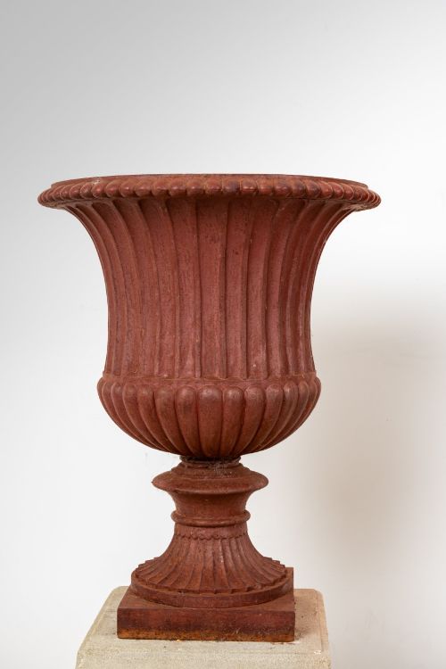 fig 3. A pair of 19th-century fluted cast iron Campana urns with rust-red finish, elevated on square carved beige stone pedestals.